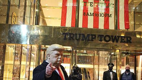 Ein Mann mit einer Trump-Maske in der Hand gestikuliert vor dem Trump Tower, der von einem Polizisten einer Spezialeinheit des NYPD auf der 5th Avenue in Manhattan am Vorabend der Präsidentschaftswahlen gesichert wird.