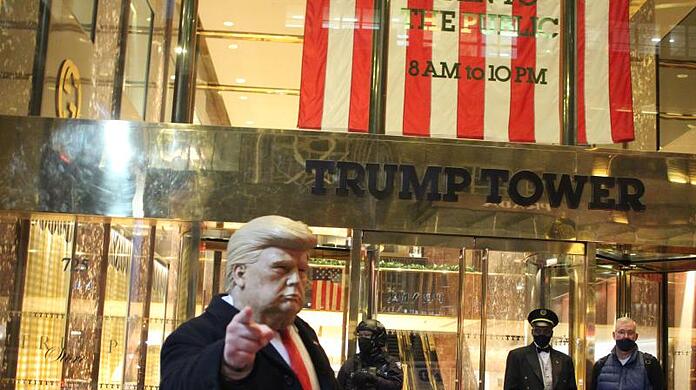 Ein Mann mit einer Trump-Maske in der Hand gestikuliert vor dem Trump Tower, der von einem Polizisten einer Spezialeinheit des NYPD auf der 5th Avenue in Manhattan am Vorabend der Präsidentschaftswahlen gesichert wird.