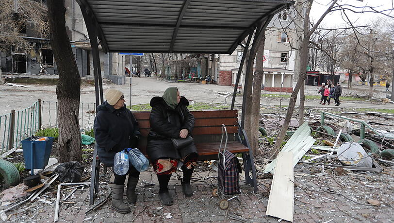Zwei Frauen sitzen an einer Haltestation in Mariupol. Mehr als 2.800 Menschen sind nach ukrainischen Angaben aus besonders umkämpften Gebieten im Osten des Landes herausgebracht worden. Etwa 2500 Flüchtlinge seien am Freitag in der Stadt Saporischschja im Süden angekommen, darunter 363 aus Mariupol, schrieb Vize-Regierungschefin Wereschtschuk auf Telegram.