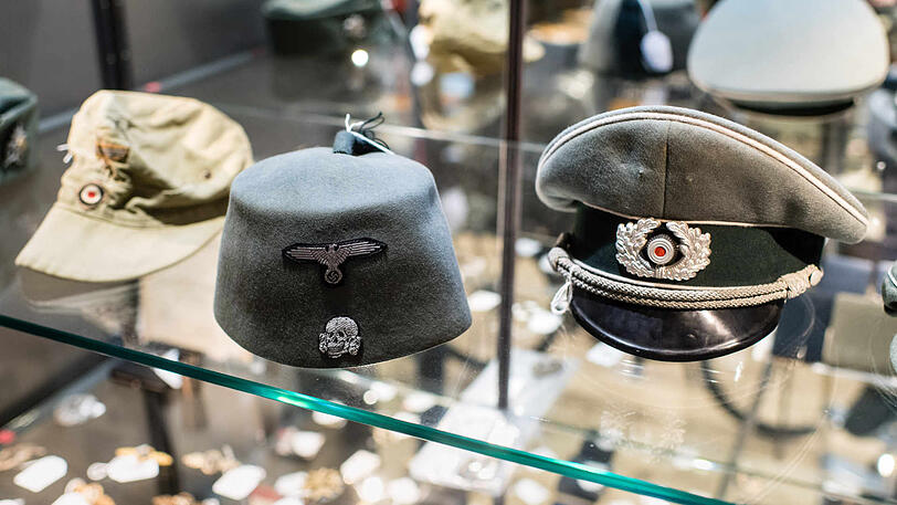 Eine Tropenfeldmütze für Mannschaften des Heeres (v.l.), eine Fez zur Felduniform der muslimischen Legionäre der Waffen-SS, eine Schirmmütze für Offiziere der Infanterie liegen in einer Vitrine im Auktionshaus "Hermann Historica".