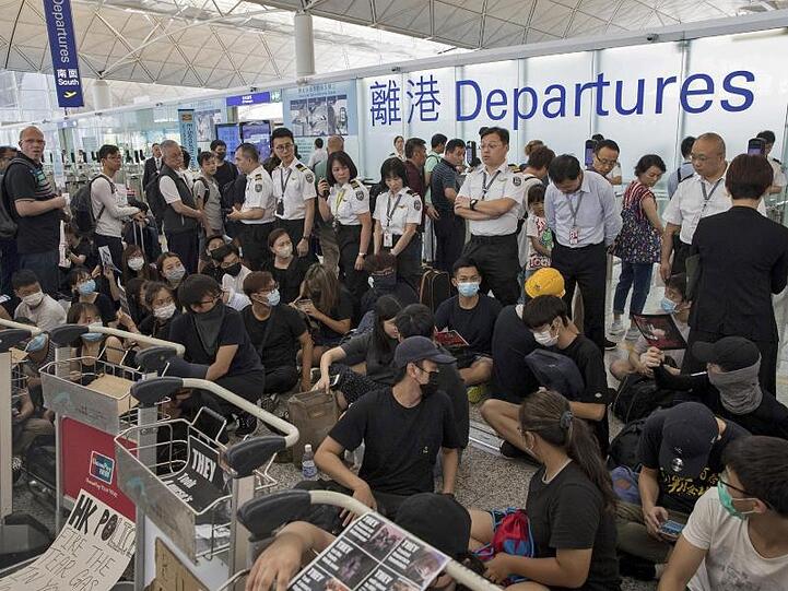 Sicherheitskräfte stehen hinter Demonstranten, die sich zu einem Sitzstreik im Terminal des Flughafens versammelt haben.