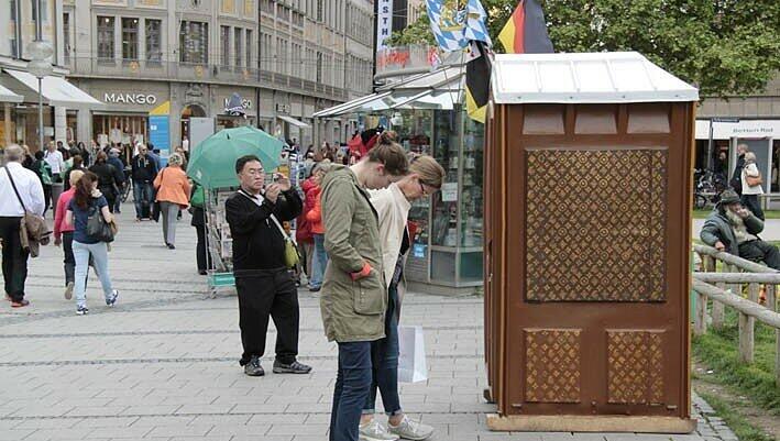...in der Fußgängerzone bleiben vor dem Häuschen mit dem braun-goldenen, an Louis Vuitton erinnernden Muster stehen. ...in der Fußgängerzone bleiben vor dem Häuschen mit dem braun-goldenen, an Louis Vuitton erinnernden Muster stehen.