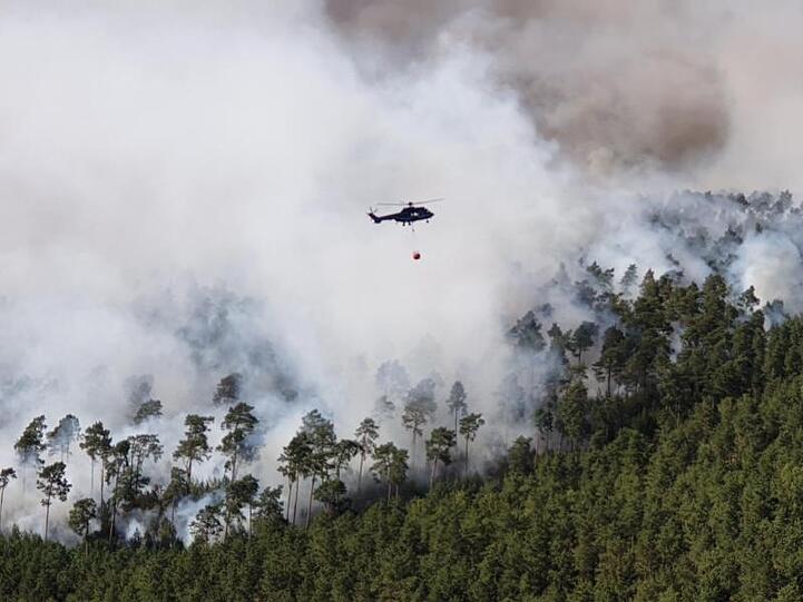 Ein Hubschrauber der Bundespolizei fliegt bei Löscharbeiten über einem Waldstück in der Lieberoser Heide.