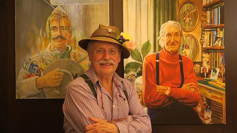 Künstler Wolfgang Prinz mit zwei seiner Werke, die in der Ausstellung zu sehen sind: ein frühes Selbstporträt (l.) und ein Gemälde des legendären AZ-Spaziergängers Sigi Sommer.