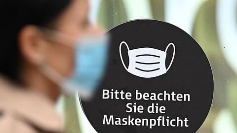 Eine Frau mit Mundschutz geht an einem Schaufenster vorbei, dass auf die Maskenpflicht hinweist.