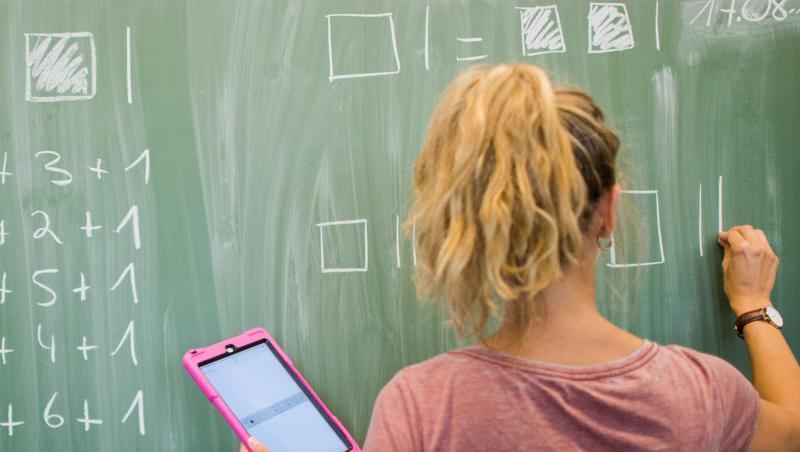 Eine Lehrerin schreibt an eine Schultafel und blickt dabei auf einen Tablet-Computer iPad. Foto: Julian Stratenschulte/Archiv Eine Lehrerin schreibt an eine Schultafel und blickt dabei auf einen Tablet-Computer iPad. Foto: Julian Stratenschulte/Archiv