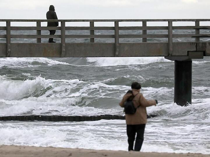 Spaziergänger sind an der aufgewühlten Ostsee unterwegs.