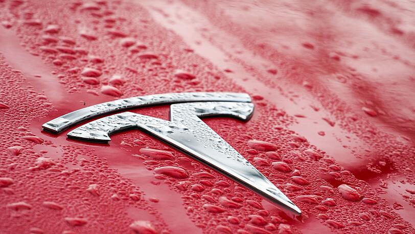 Das Logo auf der nassen Motorhaube eines roten Tesla.