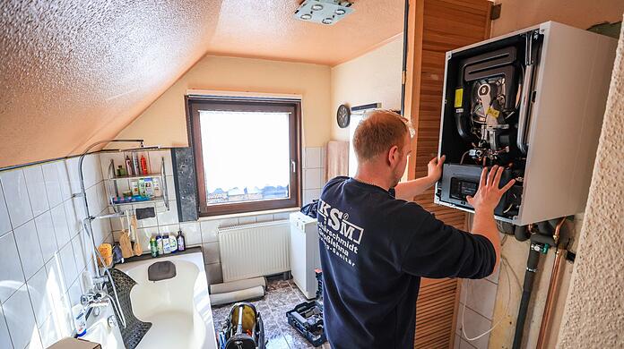 Ein Mitarbeiter einer Sanitär- und Heizungsbaufirma installiert eine moderne Gasbrennwerttherme in einem Einfamilienhaus.