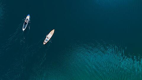 Ein Mann und eine Frau genießen das schöne Wetter mit ihren SUPs (Stand up Paddle Boards) auf dem Langwieder See.
