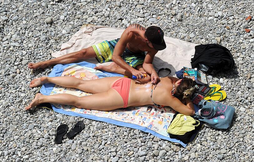 Netter Service: Ein Mann cremt an der Isar seine Begleiterin mit Sonnenschutz ein &ndash; bei dieser intensiven UV-Strahlung eine gute Idee.