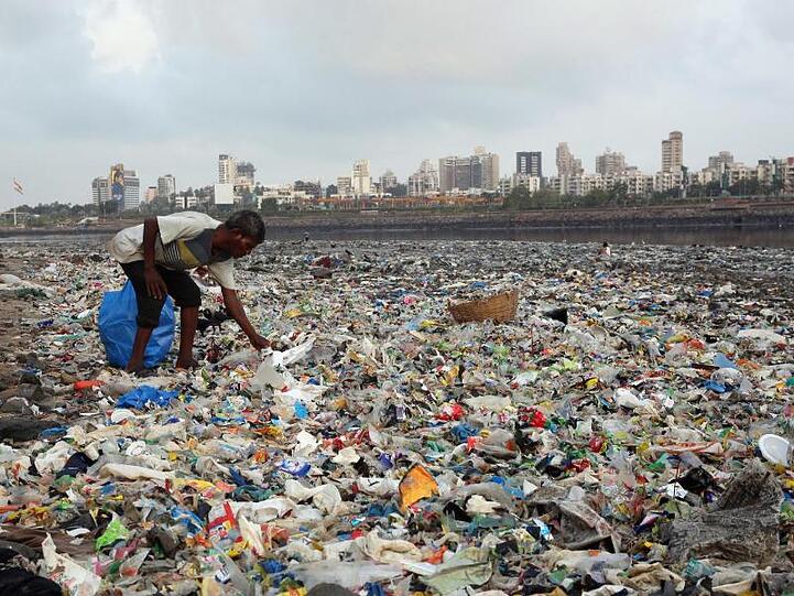 Ein Mann sammelt Plastik und andere wiederverwertbare Materialen an der von Plastiktüten und sonstigen Müll übersäten Küste vor Mumbai.