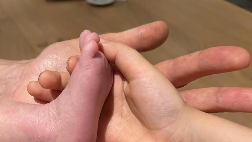 Z&auml;rtlich ber&uuml;hren die Eltern und ihre &auml;lteste Tochter den kleinen Fu&szlig; des Babys, das gesund zur Welt kommen durfte und nun viele Fu&szlig;abdr&uuml;cke in ihrem gemeinsamen Familienleben hinterlassen soll.