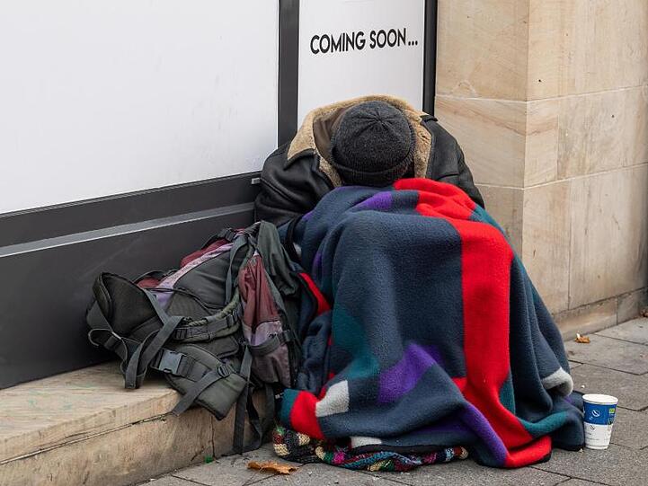 Ein Obdachloser sitzt am Straßenrand vor einem Ladengeschäft. F. Foto: Peter Kneffel/dpa