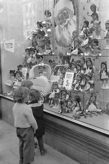 1958: Verlockend schaut sie aus, die Auslage im weihnachtlichen Schaufenster. Ob das Christkind wohl so eine Puppe bringt?
