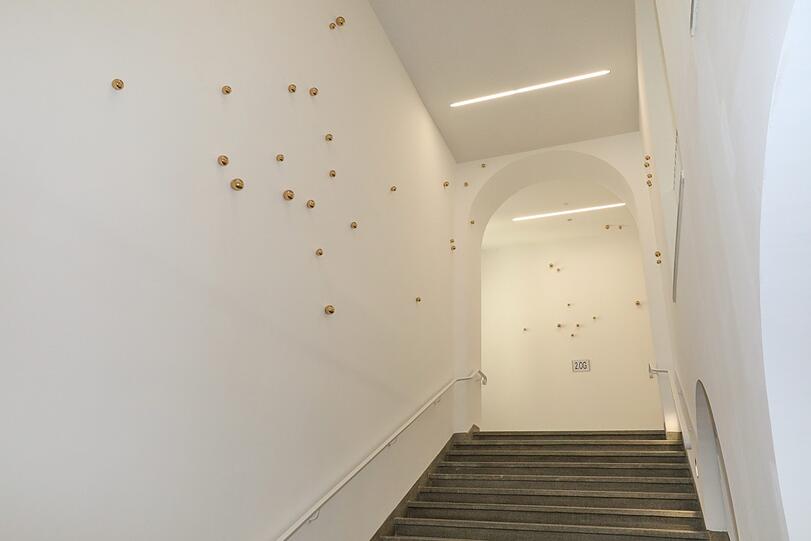 Zusammen mit Schülern und Lehrern hat die Münchner Künstlerin Gabriele Obermayer im Projekt "Kugelschwarm" 111 Bronzekugeln geformt. Sie wurden alle an der Wand aufgehangen und einen Schwarm darstellen - sinnbildlich für die Schüler der Schule.