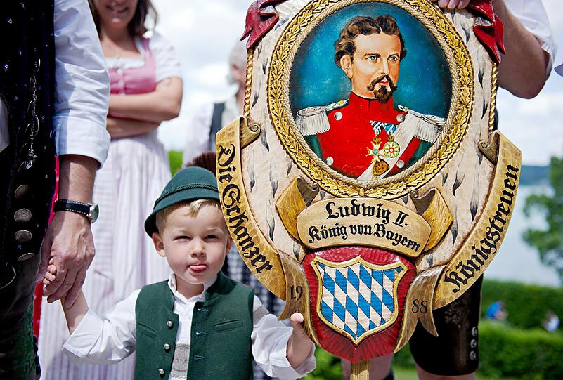 Ein kleiner Junge in Tracht neben einem Banner mit dem Konterfei von König Ludwig II.