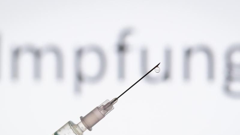 Eine Spritze wird vor den Schriftzug "Impfung" gehalten.