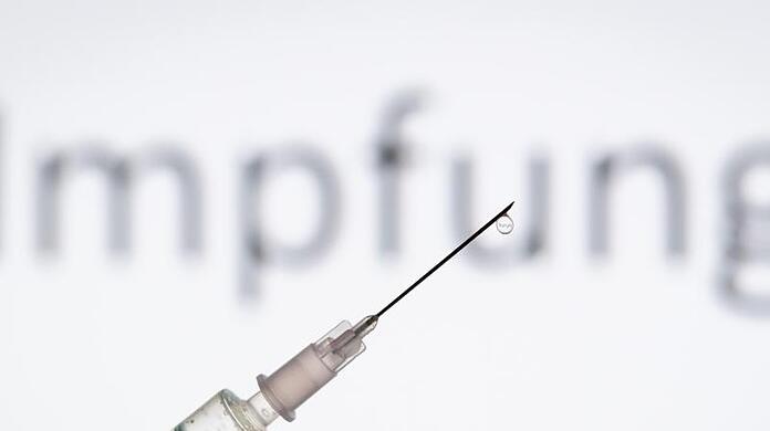 Eine Spritze wird vor den Schriftzug "Impfung" gehalten.