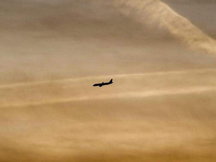 Ein Flugzeug setzt beim Sonnenaufgang zum Landeanflug an. Foto: Julian Stratenschulte/dpa/Archivbild