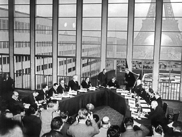 Fotografen dokumentieren den historischen Moment, in dem der britische Außenminister Anthony Eden im Oktober 1954 die Vereinbarung zum Beitritt der Bundesrepublik Deutschland in die Nato unterzeichnet.