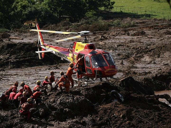 Ein Hubschrauber landet neben Feuerwehrleuten, die nach Opfern im Schlamm suchen.