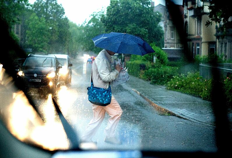 Ein Mann mit einem Regenschirm geht am 11.06.2014 in Göttingen (Niedersachsen) bei starkem Regen über eine Kreuzung.