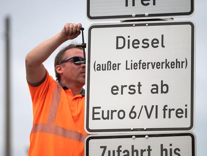 Ein Arbeiter hängt ein Schild auf, das auf ein Fahrverbot für Dieselfahrzeuge der Euronorm 5/V und schlechter hinweist.