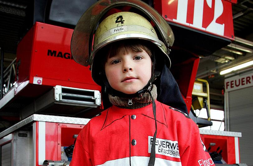 Ein kleiner Bub schlüpft schon mal in die richtige Kleidung. Mit vielen Aktionen werben Feuerwehren in Bayern um Nachwuchs.
