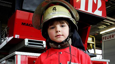Ein kleiner Bub schlüpft schon mal in die richtige Kleidung. Mit vielen Aktionen werben Feuerwehren in Bayern um Nachwuchs.