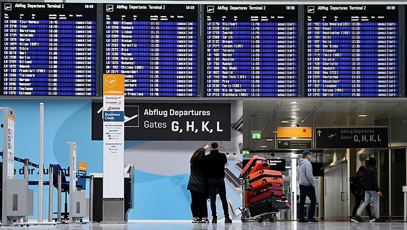 Passagiere stehen im Münchner Flughafen vor der Anzeigentafel.