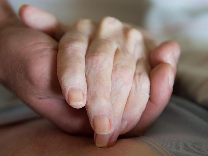 Ein Altenpfleger hält die Hand einer pflegebedürftigen Frau.