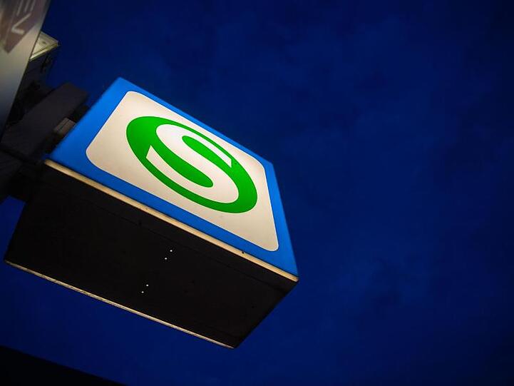 Ein S-Bahn-Schild hängt an der Station Hackerbrücke vor einem dunklen Morgenhimmel. Foto: Lino Mirgeler/dpa/Archivbild
