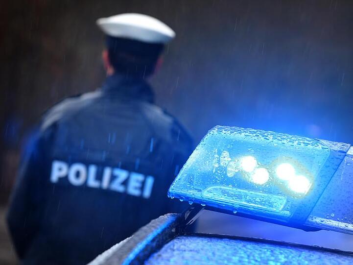 Ein Polizist steht im Regen vor einem Streifenwagen dessen Blaulicht aktiviert ist. Foto: Karl-Josef Hildenbrand/dpa/Archivbild