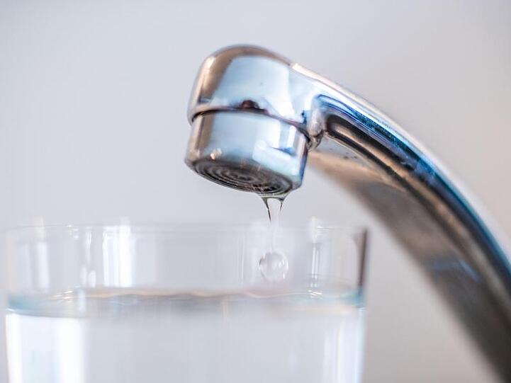 Wasser läuft aus einem Wasserhahn in ein Glas.