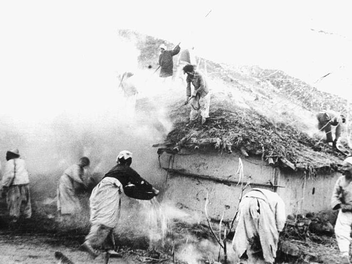 Die Bewohner eines hinter der Front gelegenen nordkoreanischen Dorfes versuchen, ihre durch Luftangriffe der UN-Streitkräfte in Brand geratenen Häuser zu löschen, aufgenommen im Februar 1951.