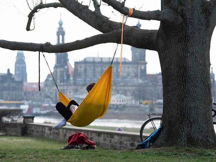 Ein Mann hat es sich am Ufer der Elbe vor der Kulisse der Dresdner Altstadt in einer Hängematte gemütlich gemacht.