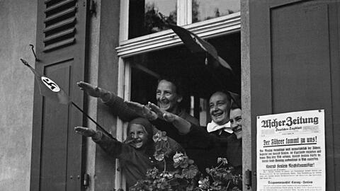 Mit Hakenkreuz-Fahnen und ausgestreckten Armen bejubelt diese Familie einen Besuch Adolf Hitlers in ihrer Heimatstadt. Ob die Frauen später mit ihren Familien über ihre Begeisterung gesprochen haben? Vermutlich haben sie eher geschwiegen.