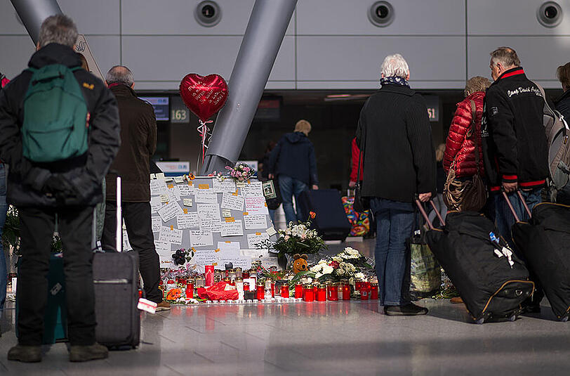 Reisende stehen am Flughafen Düsseldorf vor Blumen und Kerzen für die Opfer des Germanwings-Unglücks. Nach dem Unglück beginnt an diesem Wochenende der Osterreiseverkehr an den Flughäfen.