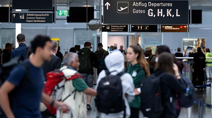 Passagiere stehen mit ihrem Gepäck vor der Sicherheitskontrolle am Flughafen München.