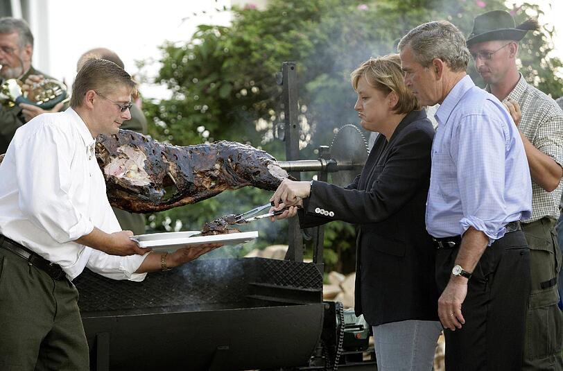 Angela Merkel (hier 2006 beim Wildschweinessen mit dem damaligen US-Präsidenten George W. Bush in Mecklenburg-Vorpommern) betont, dass die Deutschen ihre Essgewohnheiten aus Rücksicht auf Migranten nicht verändern sollten.