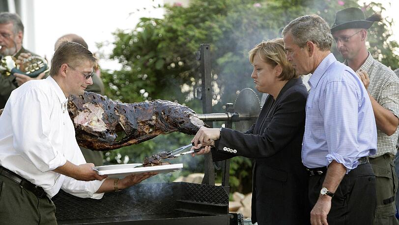 Angela Merkel (hier 2006 beim Wildschweinessen mit dem damaligen US-Präsidenten George W. Bush in Mecklenburg-Vorpommern) betont, dass die Deutschen ihre Essgewohnheiten aus Rücksicht auf Migranten nicht verändern sollten. Angela Merkel (hier 2006 beim Wildschweinessen mit dem damaligen US-Präsidenten George W. Bush in Mecklenburg-Vorpommern) betont, dass die Deutschen ihre Essgewohnheiten aus Rücksicht auf Migranten nicht verändern sollten.