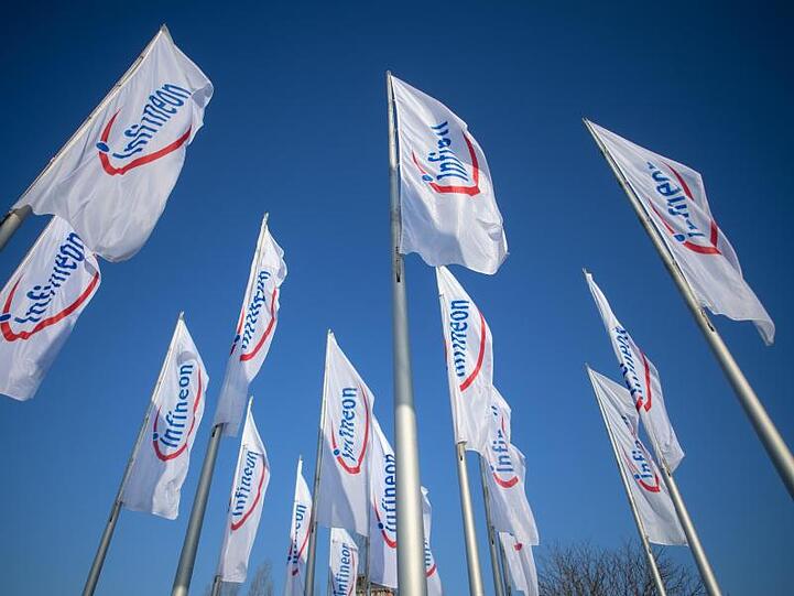 Flaggen mit dem Logo von Infineon wehen vor der Messe München im Wind. Foto: Matthias Balk/dpa/Archivbild