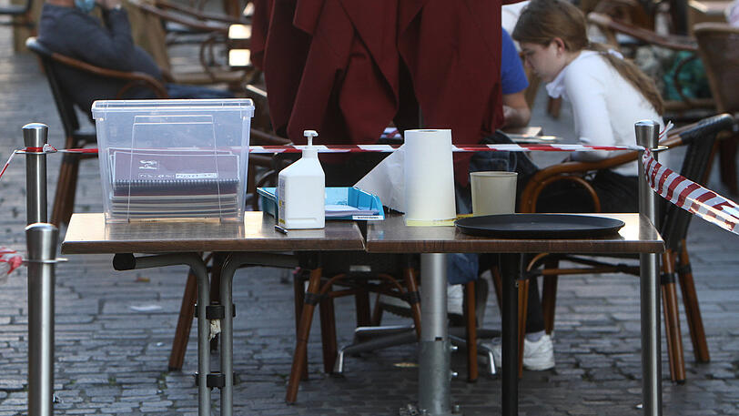 Speisekarten, Desinfektionsmittel und eine Ablage für Kontaktdaten stehen vor einem Restaurant. In Letztere hat die Polizei im Zweifelsfall Einsicht.