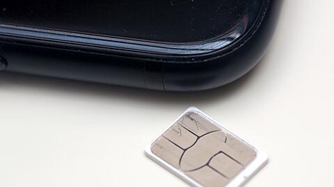 Eine SIM-Karte liegt auf einem Tisch neben einem Smartphone.