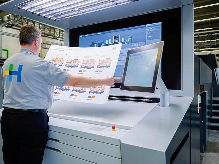 Ein Mitarbeiter hält in einer Werkshalle am Stammsitz der Heidelberger Druckmaschinen AG an einer Digitaldruckmaschine vom Typ "Primefire" einen bedruckten Bogen in den Händen.