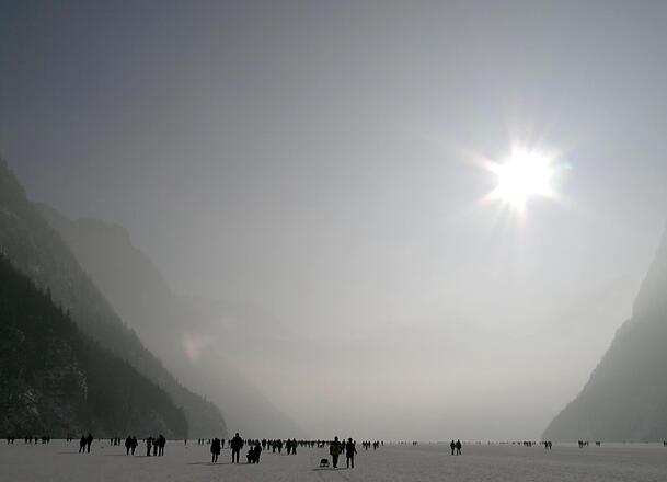 Winter 2006: Menschen spazieren &uuml;ber die weite Eisfl&auml;che des K&ouml;nigssees, die Sonne steht grell &uuml;ber dem Talkessel.