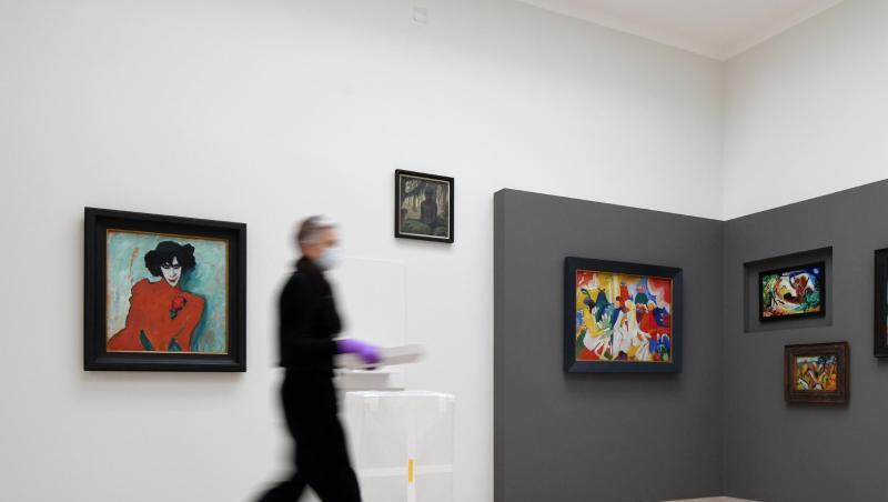 Eine Mitarbeiterin geht im Museum Lenbachhaus durch die neue Ausstellung "Gruppendynamik. Der Blaue Reiter" am Bild "Bildnis des Tänzers Alexander Sacharoff" (l) von Alexej von Jawlensky vorbei.