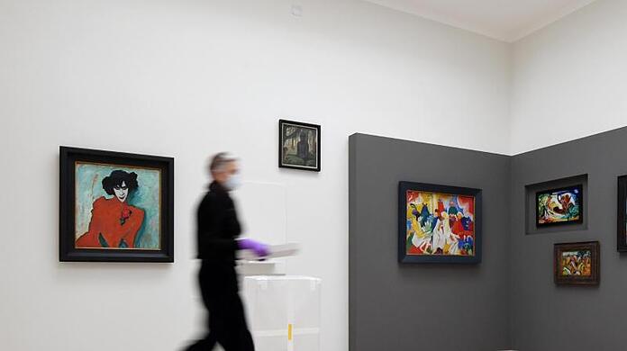 Eine Mitarbeiterin geht im Museum Lenbachhaus durch die neue Ausstellung "Gruppendynamik. Der Blaue Reiter" am Bild "Bildnis des Tänzers Alexander Sacharoff" (l) von Alexej von Jawlensky vorbei.