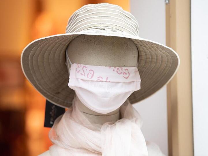 Eine Puppe mit einem Mundschutz steht am Eingang einer Boutique.